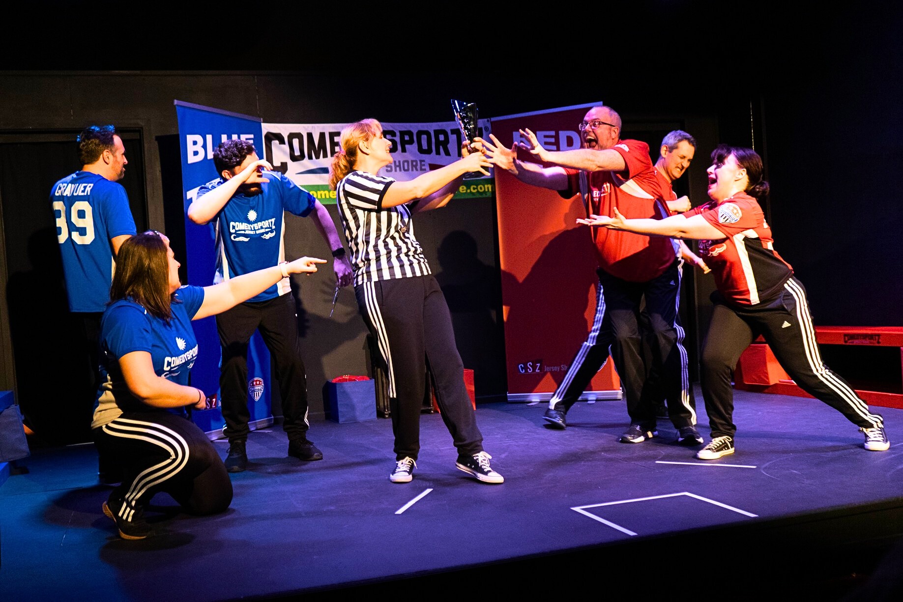 ComedySportz Jersey Shore players reaching for a trophy on stage